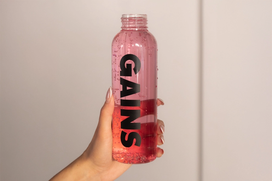 Hand holding a clear pink bottle printed with GAINS
