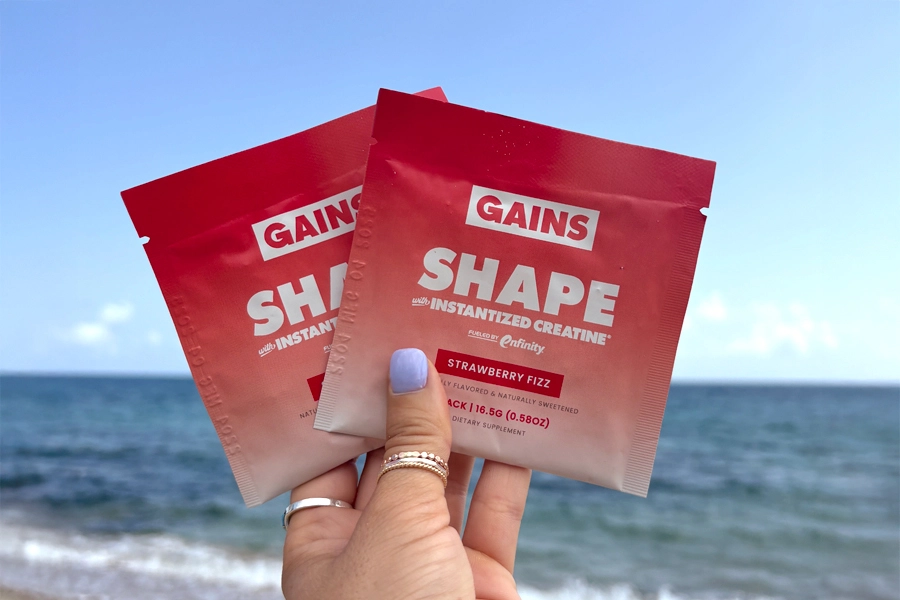 Two red SHAPE sachets held up at the beach